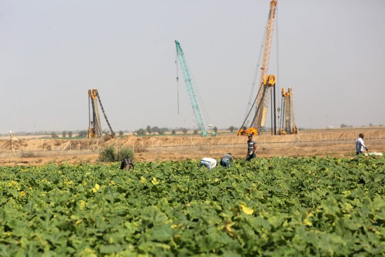 IDF equipment working on the Israel-Gaza border fence, as Gazan farmers work in the foreground.